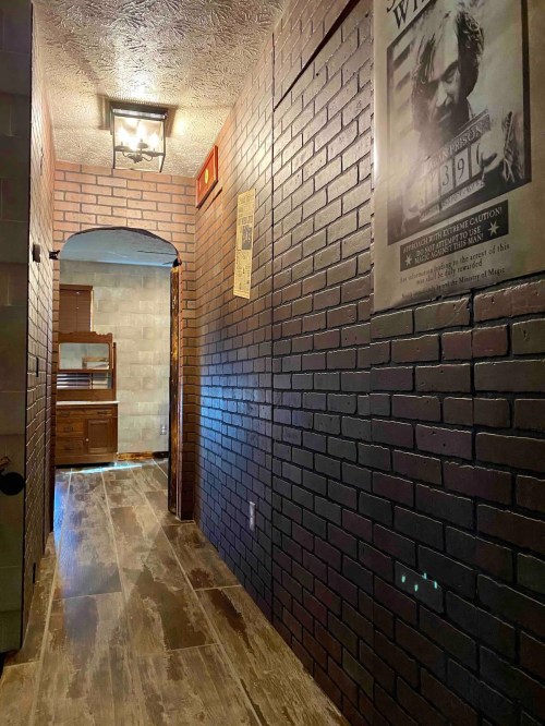A dimly lit hallway with brick walls, wooden flooring, and a vintage poster on the wall.