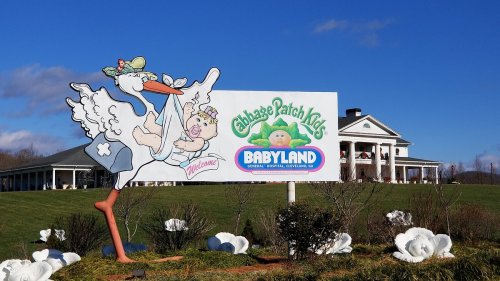 Sign for Cabbage Patch Kids Babyland, featuring a stork and a large building in the background under a blue sky.