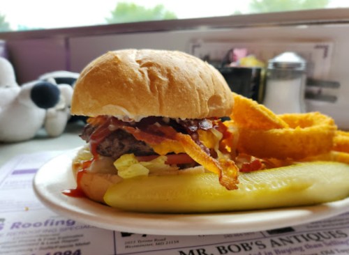 A juicy burger with bacon, cheese, lettuce, and tomato, served with curly fries and a pickle on a plate.