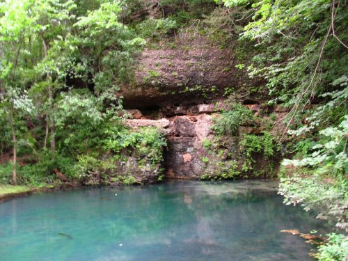 A serene pond surrounded by lush greenery and rocky cliffs, reflecting the natural beauty of the landscape.
