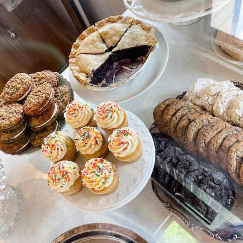 A display of assorted baked goods, including cupcakes with sprinkles, cookies, and a slice of pie.