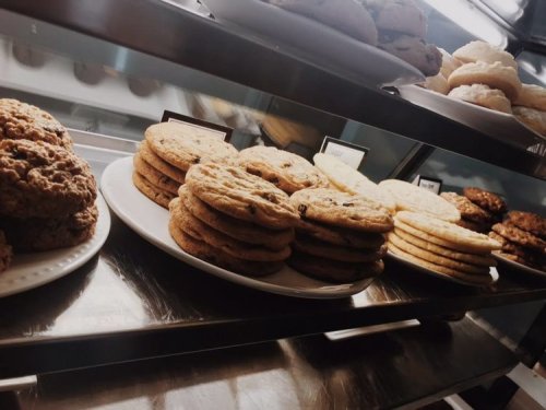 A display of various cookies on plates, including chocolate chip and oatmeal, in a bakery setting.