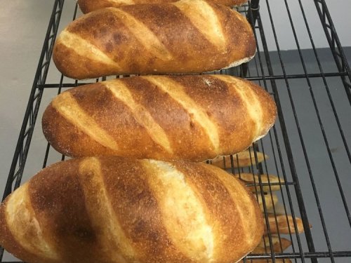 Freshly baked loaves of bread cooling on a wire rack, showcasing a golden-brown crust and diagonal scoring.