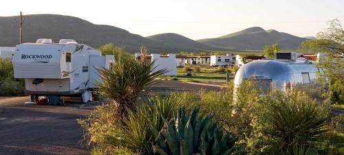 A scenic view of a campground with RVs and mountains in the background, surrounded by desert vegetation.