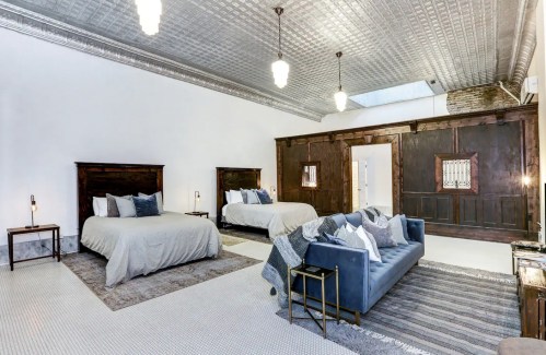 Spacious bedroom with two beds, a blue sofa, and stylish decor, featuring high ceilings and vintage lighting.