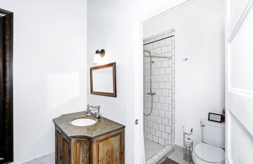 A bright bathroom featuring a wooden vanity, mirror, shower, and white tiled walls.