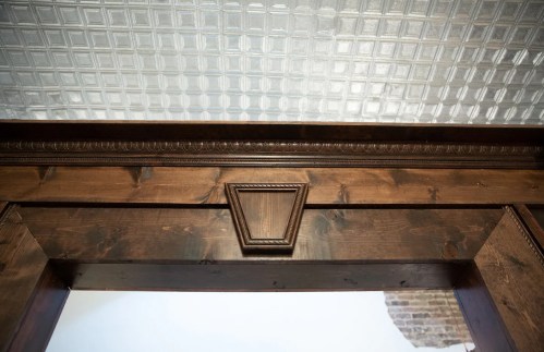 Close-up of a wooden door frame with decorative molding and a textured glass panel above.