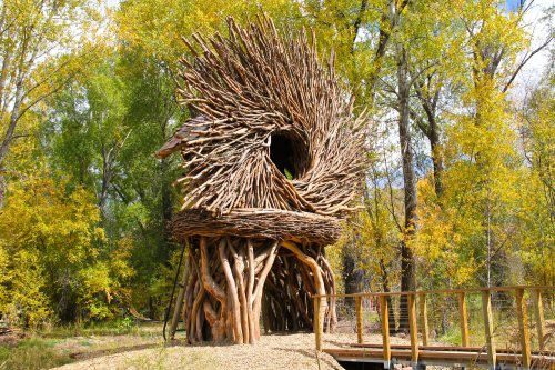 A whimsical treehouse made of intertwined branches, surrounded by vibrant autumn foliage.