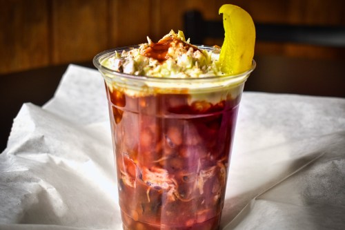 A clear cup filled with a layered mixture of beans, sauce, and topped with shredded cabbage and a lemon wedge.