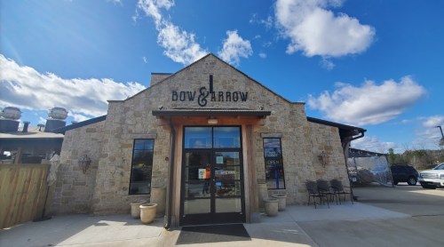Exterior of Bow & Arrow restaurant featuring a stone facade, large entrance, and blue sky with clouds.