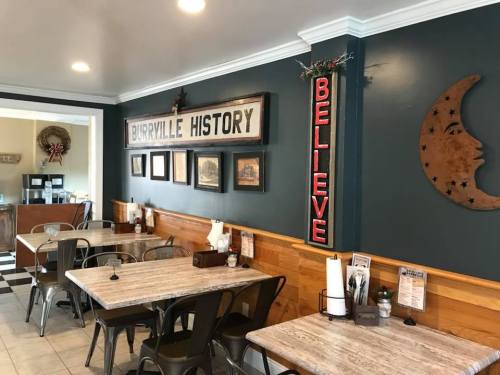 Cozy café interior with wooden tables, vintage decor, and a "Believe" sign on the wall.