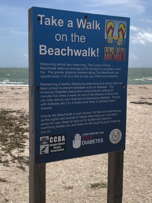 Sign promoting the Corpus Christi Beachwalk, highlighting its benefits for health and diabetes prevention.