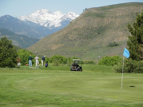 A scenic golf course with a flag, mountains in the background, and golfers preparing to tee off.