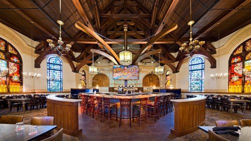 Elegant restaurant interior featuring high wooden ceilings, stained glass windows, and a central bar area with seating.
