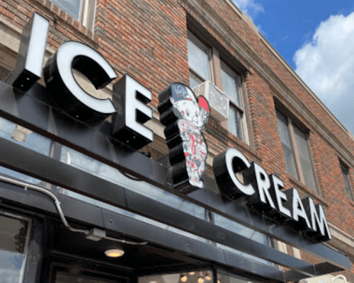 Sign for an ice cream shop featuring a cartoon character, set against a brick building with a blue sky.