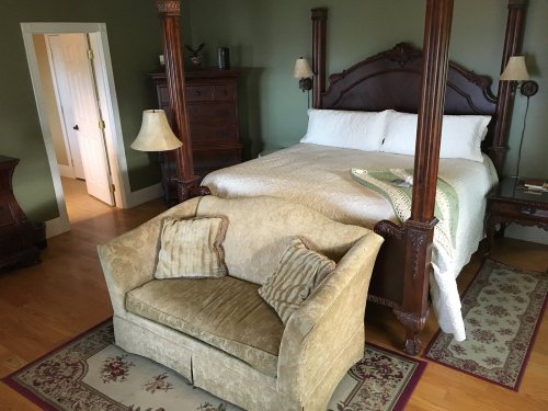 A cozy bedroom featuring a four-poster bed, a small sofa, and wooden furniture against a green wall.