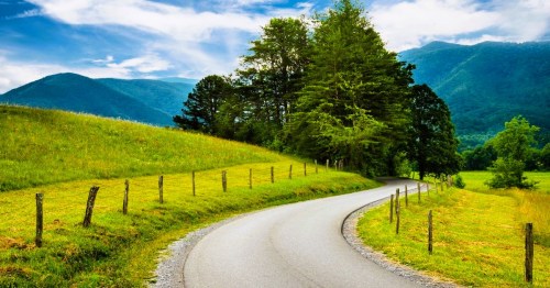Cades Cove Loop Road with mountain views in Tennessee, surrounded by reen fields and trees, under a partly cloudy sky.