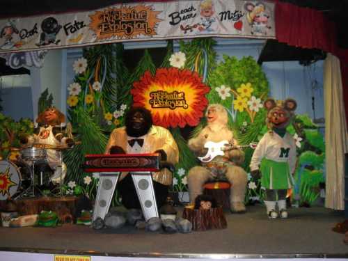 A colorful stage with animatronic characters performing music, featuring a gorilla on keyboard and a yeti with a guitar.