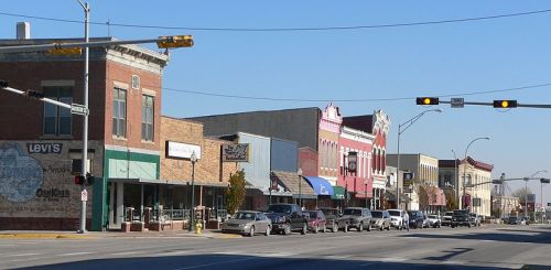 A small town street lined with historic buildings, shops, and parked cars under a clear blue sky.