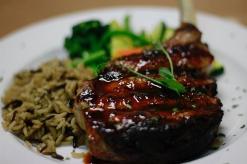 A plate featuring a grilled pork chop with barbecue sauce, served with rice and mixed vegetables.