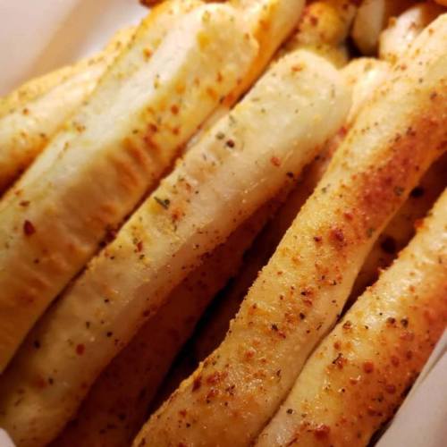 Close-up of seasoned, golden-brown breadsticks with a sprinkle of spices, arranged in a white container.