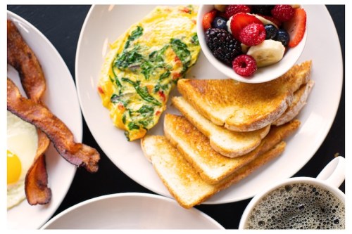 A breakfast plate featuring an omelet, toast, fresh fruit, and a cup of coffee.
