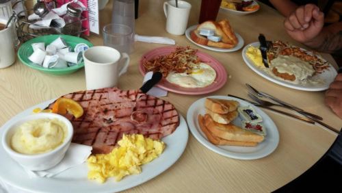 A table set with two breakfast plates: one with ham, eggs, and toast; the other with hash browns and biscuits.