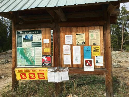 A wooden information board displaying various wilderness and fire restriction notices in a natural setting.