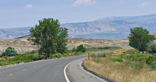 A winding road through a dry landscape with sparse vegetation and distant mountains under a clear blue sky.