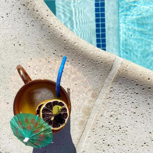 A refreshing cocktail with a lemon slice and a small umbrella, resting on a textured surface by a pool.