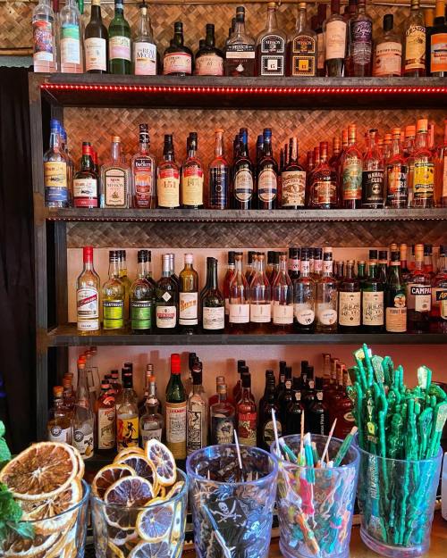 A vibrant bar shelf filled with various bottles of liquor and colorful cocktail garnishes in clear glasses.