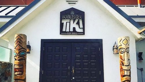 Entrance of Bootlegger Tiki in Palm Springs, featuring tiki totems and a dark double door.