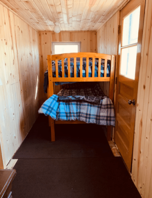 A cozy room with wooden walls, featuring a bunk bed and a door leading outside.