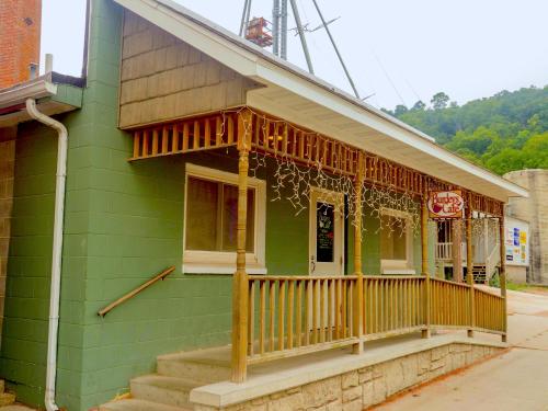 A green building with a wooden porch and string lights, featuring a sign for "Burger Cafe." Trees in the background.