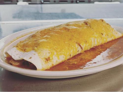A large cheese-covered burrito on a plate, smothered in red sauce, with a glossy finish.