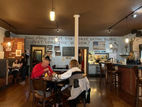 A cozy restaurant interior with wooden decor, patrons dining, and a motivational quote on the wall.