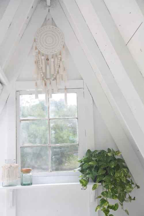 A cozy corner with a macramé wall hanging, a window, and a green plant in a bright, white room.