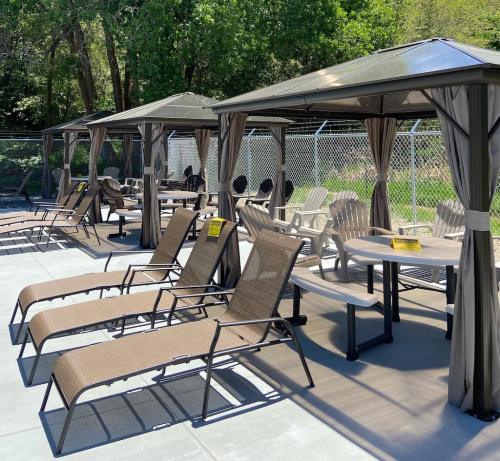 A row of poolside cabanas and lounge chairs under a sunny sky, surrounded by greenery and a fence.