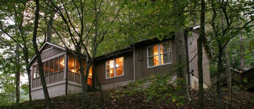 A cozy cabin nestled among trees, with warm lights glowing from the windows at dusk.