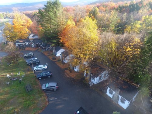 Aerial view of a quaint lodging area surrounded by colorful autumn trees and parked cars.