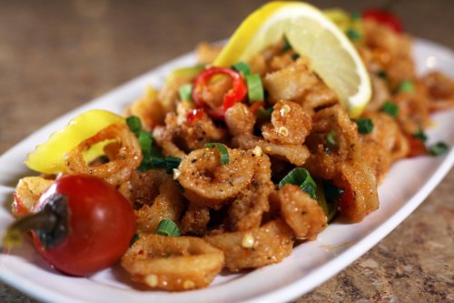 A plate of crispy fried calamari garnished with lemon slices, chili peppers, and green onions.