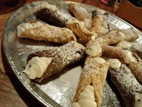 A platter of cannoli filled with creamy filling and dusted with powdered sugar.