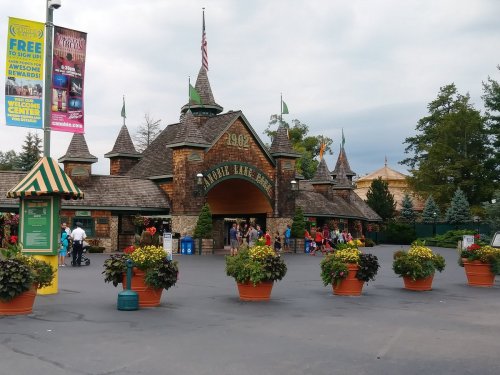 Entrance to a theme park with a castle-like structure, surrounded by colorful flower pots and visitors.