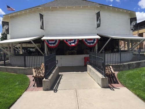 A white building with patriotic bunting, benches, and a pathway leading to it, set against a blue sky.