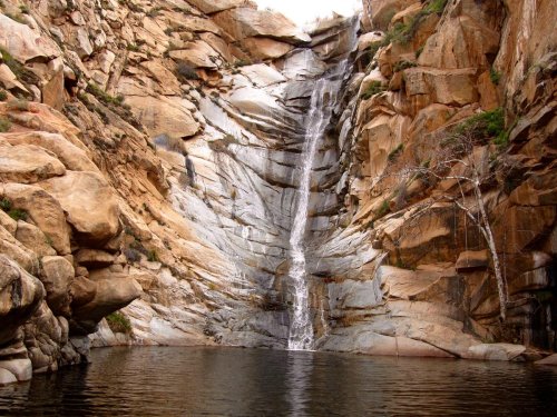 A serene waterfall cascading down rocky cliffs into a calm pool of water below, surrounded by rugged terrain.