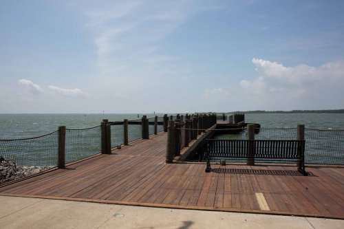 A wooden pier extends into the water, with a bench nearby and a calm sea under a blue sky.
