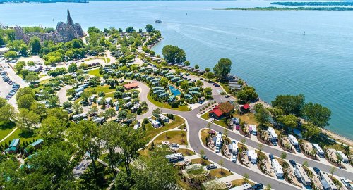 Aerial view of a lakeside RV park with numerous campers, trees, and water in the background.
