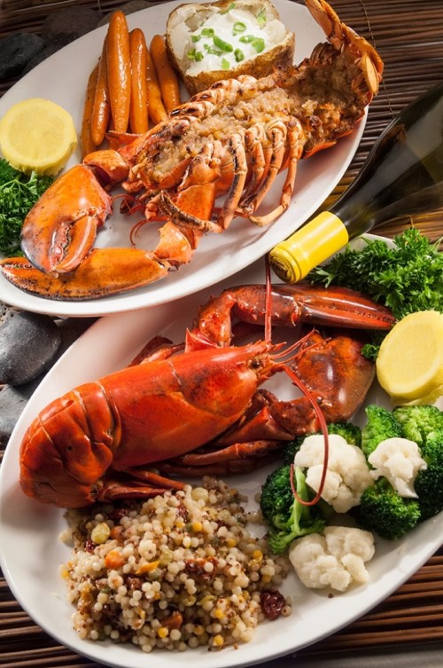 A delicious seafood platter featuring lobster, vegetables, and a side of couscous, garnished with lemon and herbs.