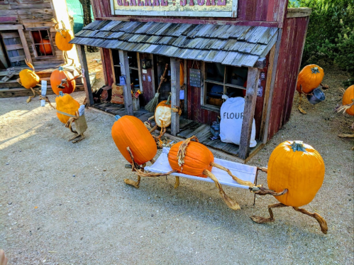 A whimsical scene of pumpkins on legs pulling a cart, in front of a rustic building with a sign that says "FLOUR."