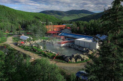 A scenic view of a hot spring resort surrounded by lush greenery and mountains under a cloudy sky.